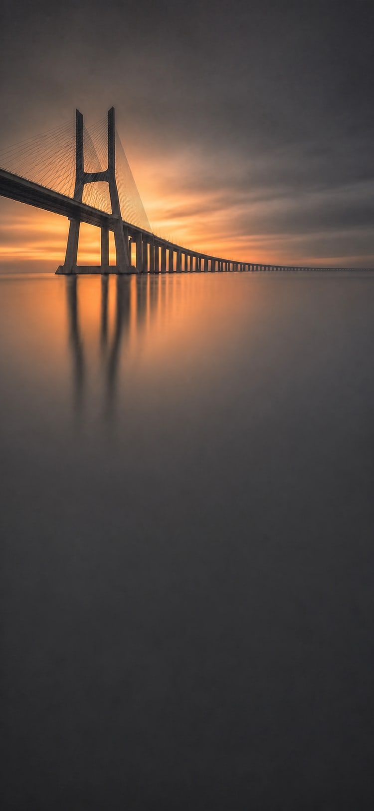 The Vasco da Gama Bridge receding across the Tagus at dusk.